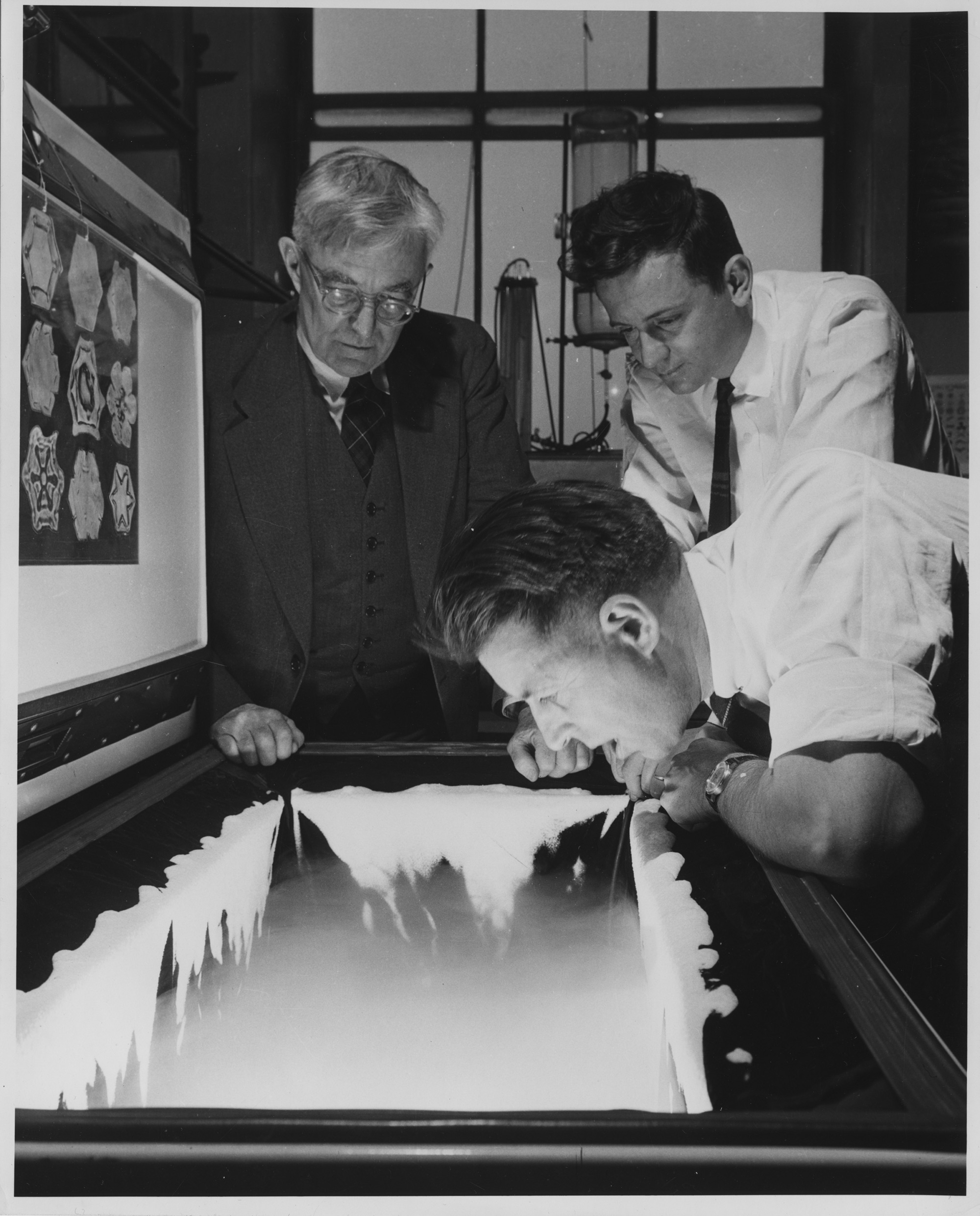 GE scientist Vincent Schaefer breathes a cloud into a freezer as colleagues Irving Langmuir and Bernard Vonnegut look on.
